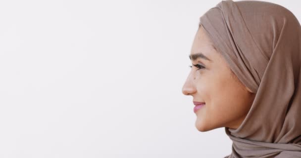 Beauté musulmane. Portrait de profil de dame islamique en hijab regardant l'espace de copie et souriant, fond blanc — Video