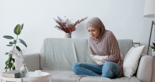 Wanita Muslim yang menderita sakit perut, periode kram, duduk sendirian di sofa di rumah — Stok Video