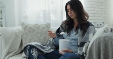 Stres yeme konsepti. Dondurma yiyen ve evde sıcak ekose altında ağlayan, ayrılık sürecinden geçen üzgün bir kadın.