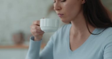 Melankolik genç bir kadının çay içerken, sıcak içecekle bardağı tutarken, depresyondan acı çekerken görüntüsü.