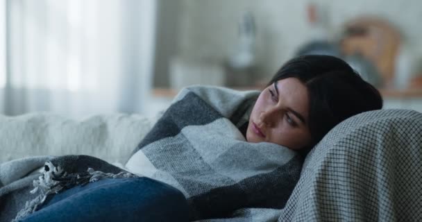 Sorgsen deprimerad ung kvinna liggande ensam på soffan insvept i rutig, trött ensam sårbar och svag — Stockvideo