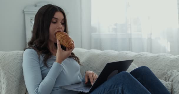 Úzkostlivá tisíciletá dáma, která se vyrovnává se stresem prostřednictvím nezdravého jídla, pracuje na laptopu a jí croissant, zpomaluje — Stock video