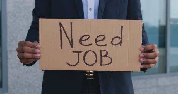 Nezaměstnaný černoch s plakátem NEED WORK stojící venku v kancelářské budově, zblízka, stopa záběru — Stock video