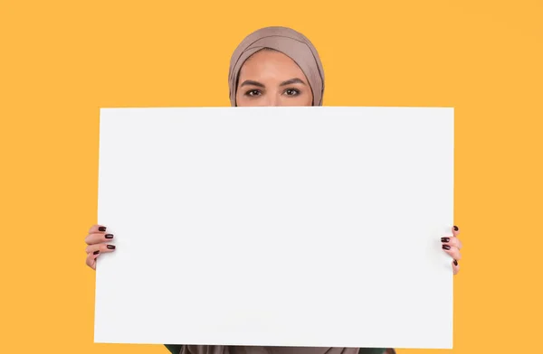 Mujer islámica en Hijab sosteniendo cartel vacío sobre fondo amarillo — Foto de Stock