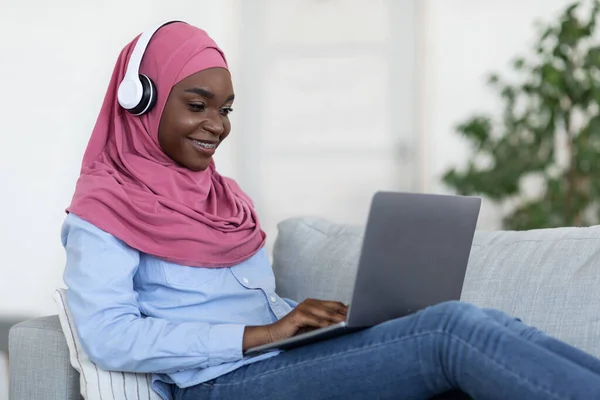 Black Muslim Woman In Hijab Studying With Laptop And Headphones At Home