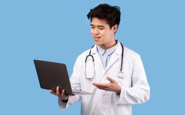 Asyalı doktor dizüstü bilgisayar tutuyor, hastayla görüntülü görüşme yapıyor.