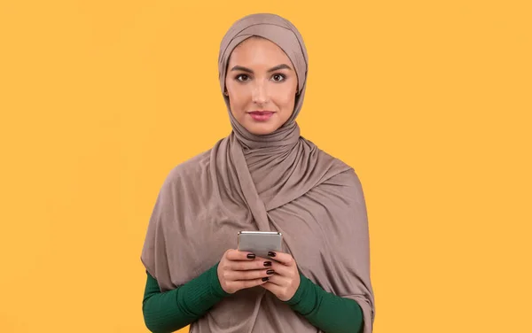 Wanita Muslim Dengan Smartphone Berdiri Pada Latar Belakang Studio Kuning — Stok Foto