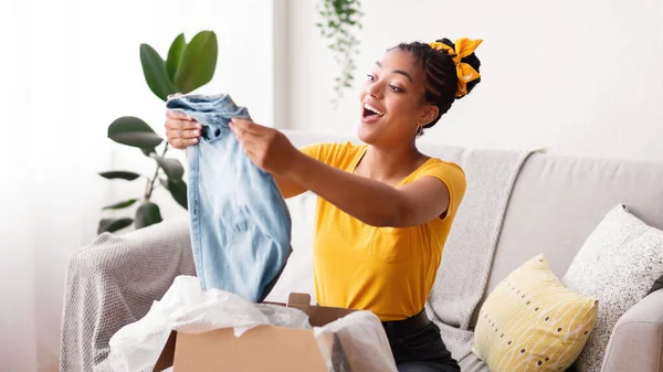 Ευτυχισμένη μαύρη γυναίκα ξεπακετάρει ρούχα μετά από online ψώνια — Φωτογραφία Αρχείου