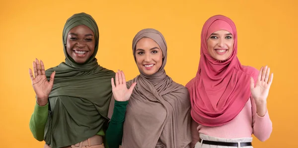 Three Muslim Ladies Waving Hello Gesture Over Yellow Background, Panorama — Stock Photo, Image