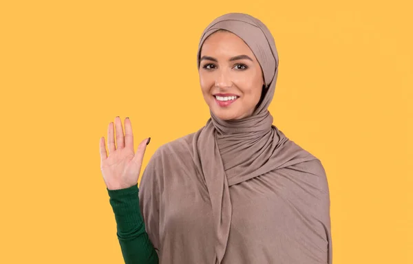 Muslimská dáma mává rukou gesto Dobrý den pozdrav na žlutém pozadí — Stock fotografie