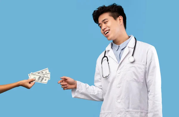 Kapzsi ázsiai férfi orvos kenőpénzt fogad el női betegtől — Stock Fotó