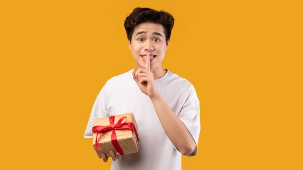 Asiático hombre celebración regalo caja, mostrando silencio signo —  Fotos de Stock