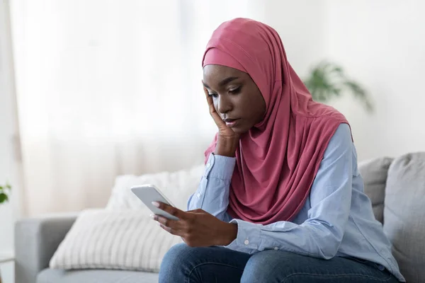 Triste dama islámica negro en hijab mensaje de lectura en el teléfono inteligente en casa — Foto de Stock