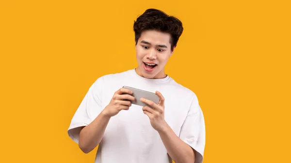 Excité asiatique homme jouer à des jeux mobiles sur fond orange — Photo