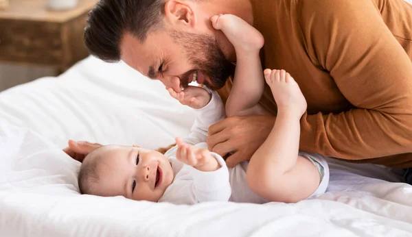 Pai abraçando ligação com pequeno bebê deitado na cama interior — Fotografia de Stock