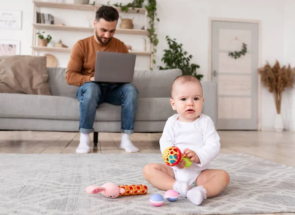 Bebê sentado brincando com brinquedos enquanto o pai trabalhava em casa — Fotografia de Stock