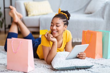 Evde tablet ve kredi kartı kullanan siyah bir kadın.