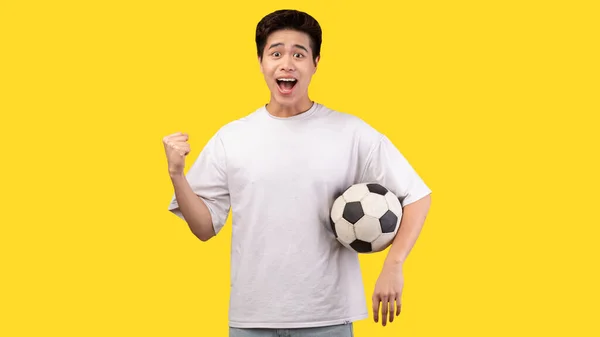 Asiatico uomo posa con calcio palla su sfondo giallo — Foto Stock