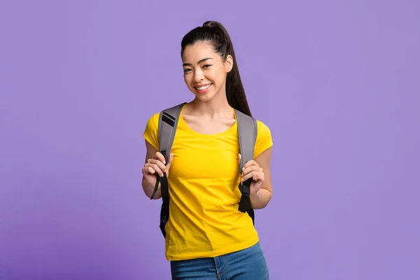 Junge schöne asiatische Studentin mit Rucksack posiert über lila Studiohintergrund — Stockfoto