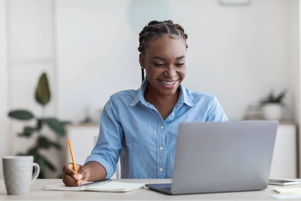 Educação online. Jovem estudante negra usando laptop em casa, tomando notas — Fotografia de Stock