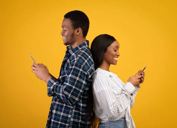 Sorrindo jovem afro-americano cara e senhora ficar de volta para trás, digitando em smartphones — Fotografia de Stock