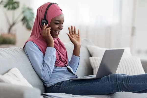 Videogesprek. Vrolijke Afrikaanse moslim vrouw in headset met behulp van laptop thuis — Stockfoto