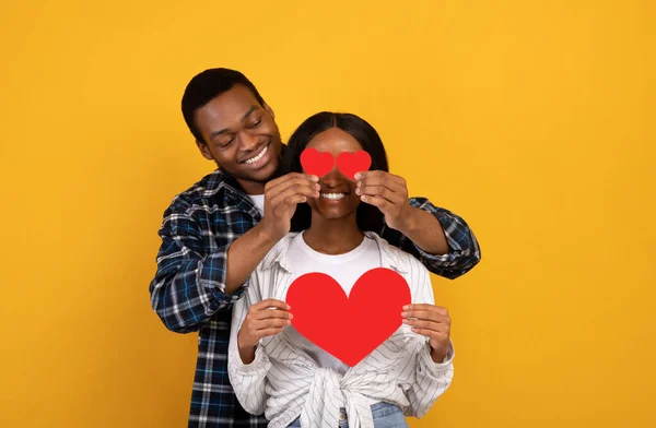 Feliz joven afroamericano hombre pone corazones a los ojos femeninos, señora sostiene el corazón — Foto de Stock