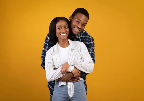 Cheerful young african american male and female in casual, hugging and looking at camera — Stock Photo, Image