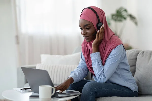 Zwarte moslim vrouw in hidjab studeren met laptop thuis, met behulp van headset — Stockfoto