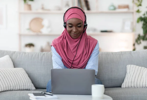 Sonriente negro musulmán freelancer dama trabajando con portátil y auriculares en casa — Foto de Stock