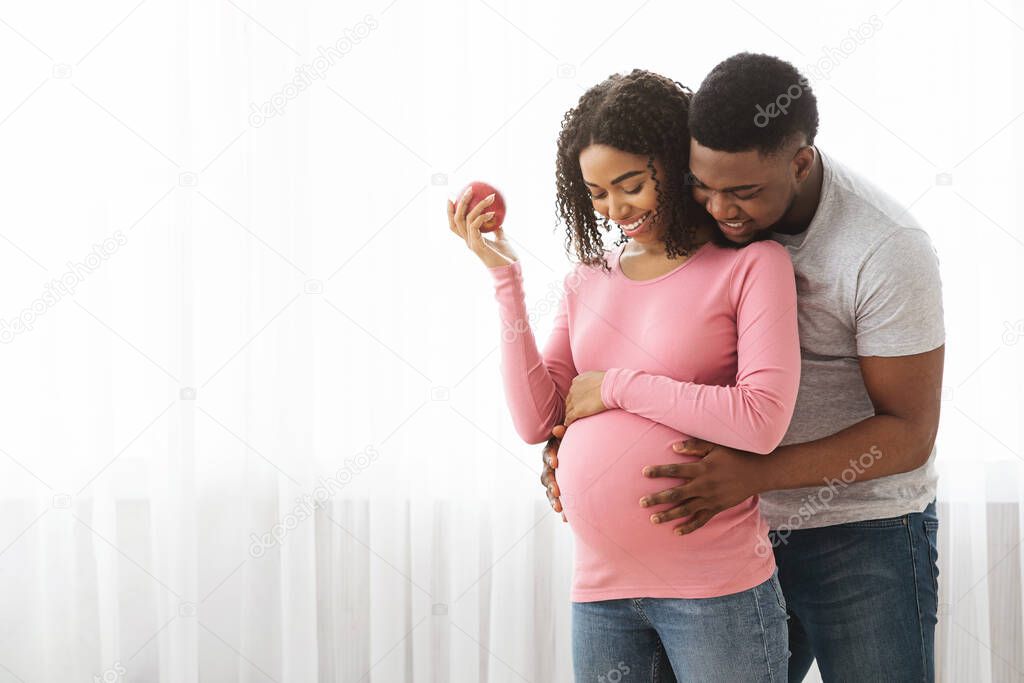 Lovely black family expecting baby, standing by window