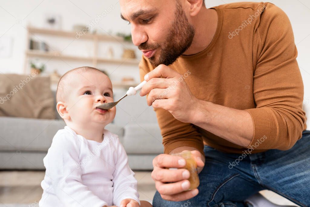 Young Father Feeding Little Baby Son With Spoon At Home