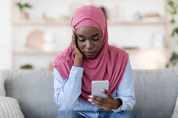 Aggódó fekete muszlim nő ül okostelefonnal a kezében otthon — Stock Fotó