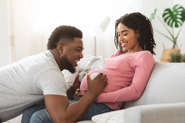 Zwarte vader houdt headset op zwangere vrouw buik — Stockfoto