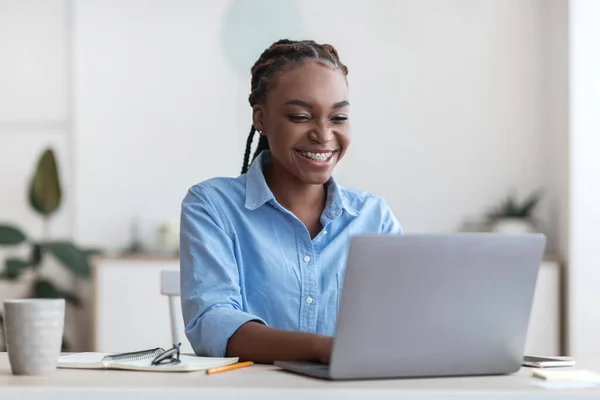 Χαμογελώντας νεαρή μαύρη εκπαιδευόμενη γυναίκα κάθεται στο χώρο εργασίας στο νέο γραφείο — Φωτογραφία Αρχείου