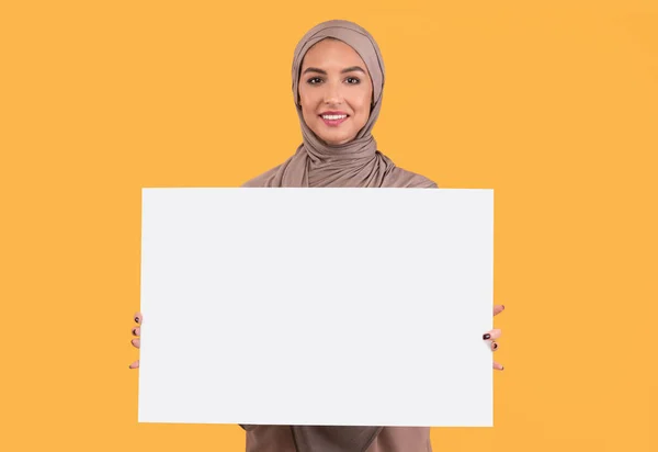 Señorita musulmana sosteniendo cartel en blanco para texto sobre fondo amarillo — Foto de Stock