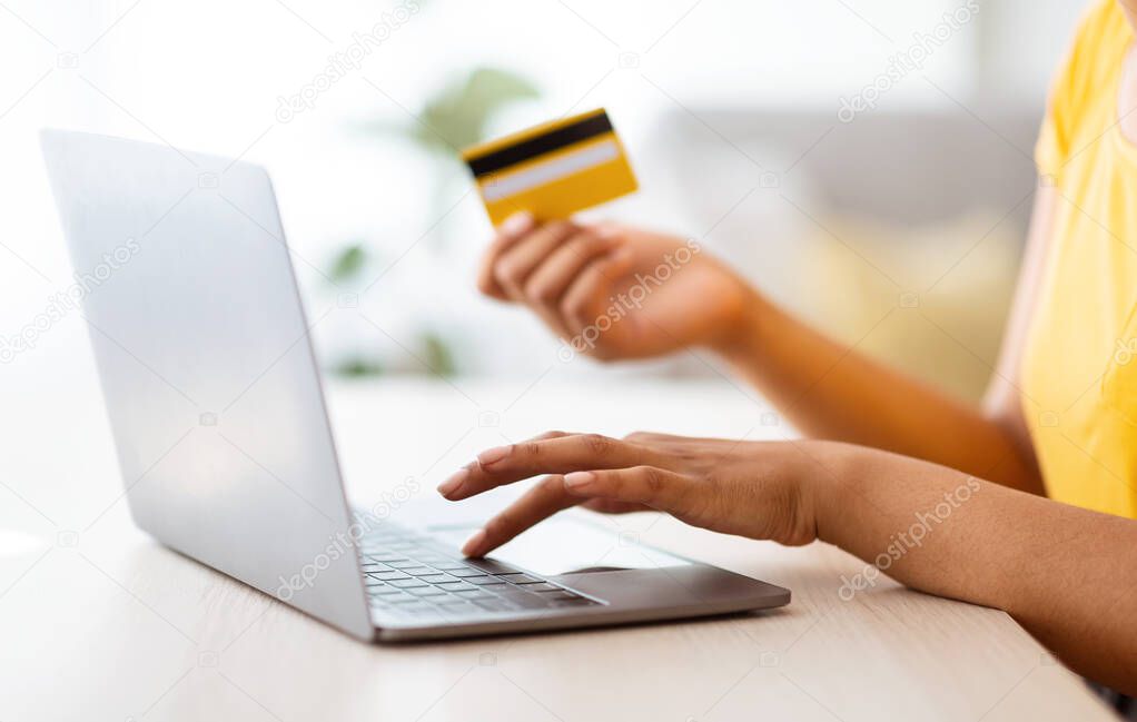 Black woman using laptop and credit card sitting at desk