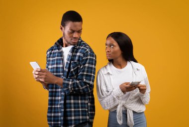 Üzgün Afrikalı Amerikalı karı koca birbirine öfke ve inançsızlıkla bakıyor ve telefonlarını tutuyor.