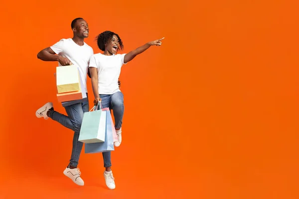 Black man and woman with purchases, pointing at empty space