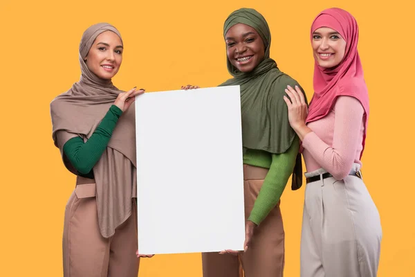 Tiga Wanita Muslim Dalam Hijab Memegang Poster Kosong, Latar Belakang Kuning — Stok Foto