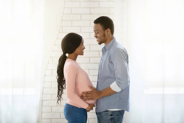 Krásná černošky těhotná žena a její manžel dívá na sebe s láskou doma, boční pohled — Stock fotografie