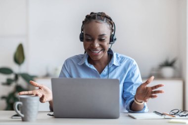 Web Konferansı. Siyah kadın çalışan, kulaklıklı. Bilgisayarla video görüşmesi yapıyor.