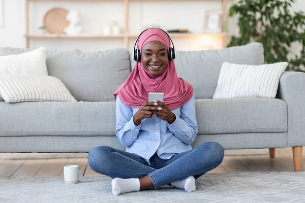 Mujer musulmana negra escuchando música en Smartphone y bebiendo té en casa —  Fotos de Stock