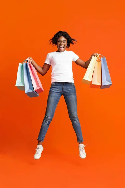 Aufgeregte schwarze Dame mit Einkaufstüten springt auf — Stockfoto