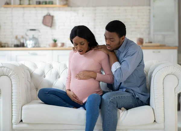 Mulher negra grávida sentindo dor, dando à luz a criança, tendo contrações enquanto marido chamando médico no telefone — Fotografia de Stock
