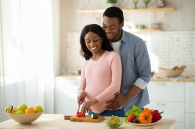 Güzel siyah hamile çift mutfakta sebze salatası yapıyor.