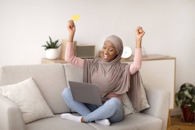 Büyük satış konsepti. Kredi kartı ve dizüstü bilgisayarla internetten alışveriş yapan tesettürlü zenci bir kadın.