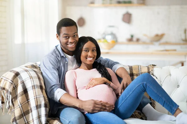 Bonito casal grávida abraçando no sofá em casa — Fotografia de Stock