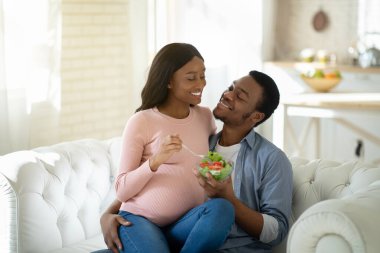 Hamilelik konseptinde dengeli diyet. Yakışıklı siyahi adam sevgili müstakbel karısına içeride lezzetli sebze salatası veriyor.