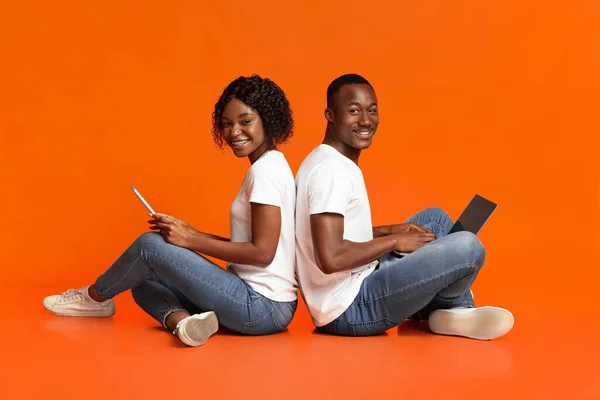 Cheerful black couple using social media over orange